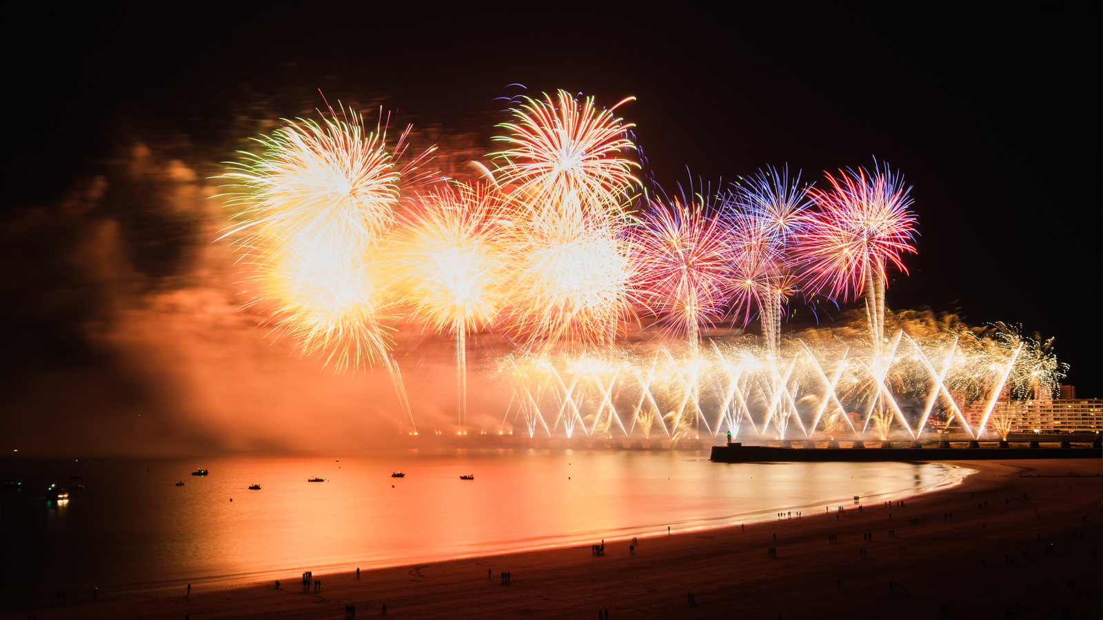 Feu d’artifice tiré au-dessus de la Grande Plage en bord de mer, avec des gerbes lumineuses colorées illuminant le ciel nocturne et se reflétant sur l’océan, lors d’un événement estival en Vendée selectionné par Parent Cool. 